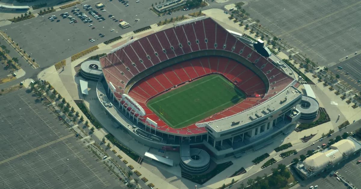Arrowhead Stadium in Kansas City An aerial view of Arrowhead Stadium in Kansas City, its open bowl ringed with deep red seats around a green football field. Wide parking lots surround the stadium on all sides.