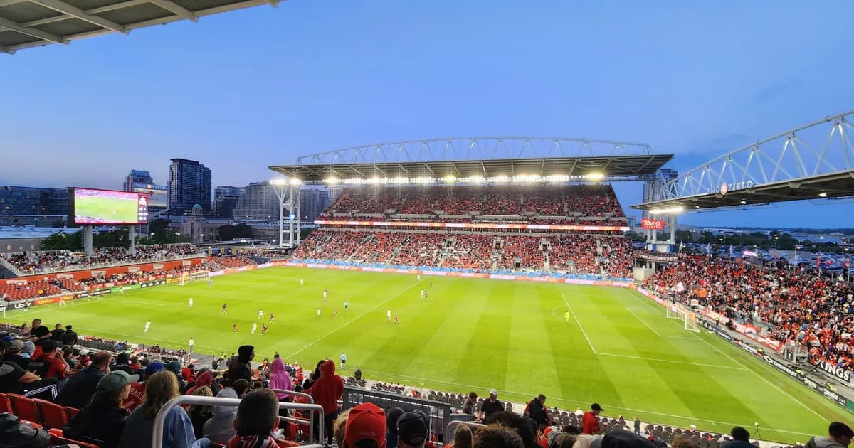 BMO Field in Toronto A view from the stands of BMO Field in Toronto at dusk, fans in red filling the seats around a striped green pitch. The Toronto skyline rises behind the open end of the stadium.