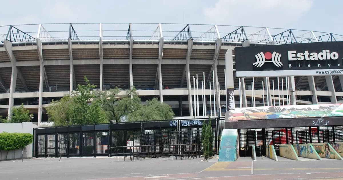 Estadio Azteca in Mexico City A street-level view of Estadio Azteca in Mexico City, its huge curved concrete bowl rising behind a black Estadio Azteca welcome sign and entrance gates. Trees and an empty forecourt sit in front of the stadium.
