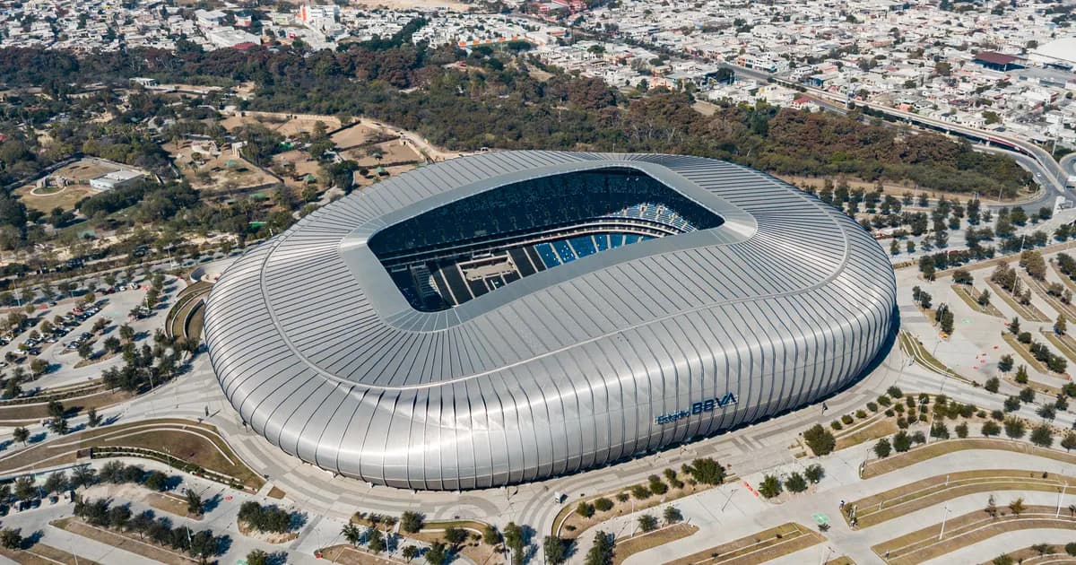 Estadio BBVA near Monterrey, Mexico An aerial view of Estadio BBVA near Monterrey, Mexico, a sleek silver oval stadium with a louvred metal shell and an open roof over its seats. Streets, homes and wooded hills surround the stadium.